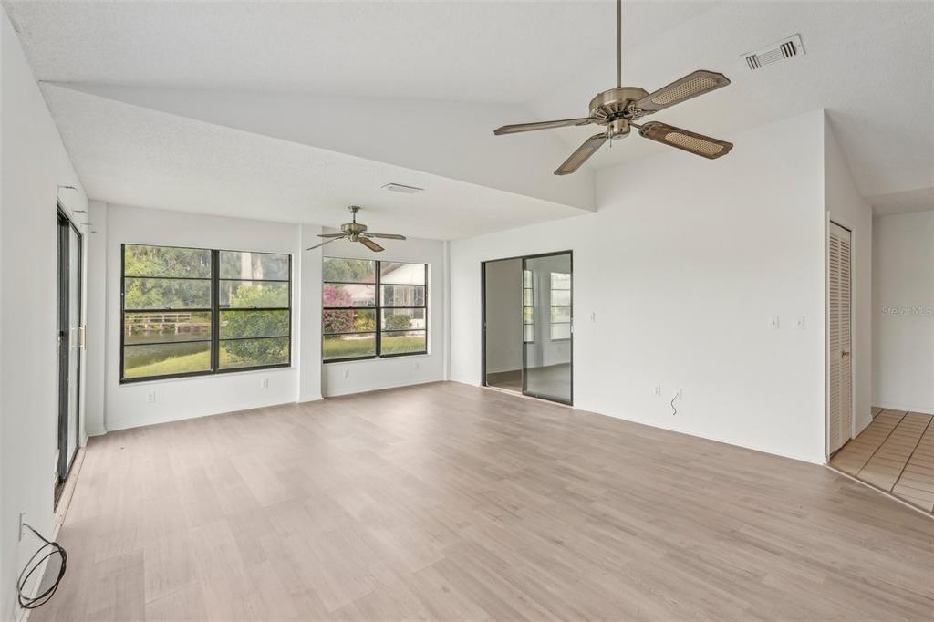 A bright living room features light wood-look flooring, vaulted ceilings, two ceiling fans, and windows — 1613 COMFY COURT, SUN CITY CENTER, FL