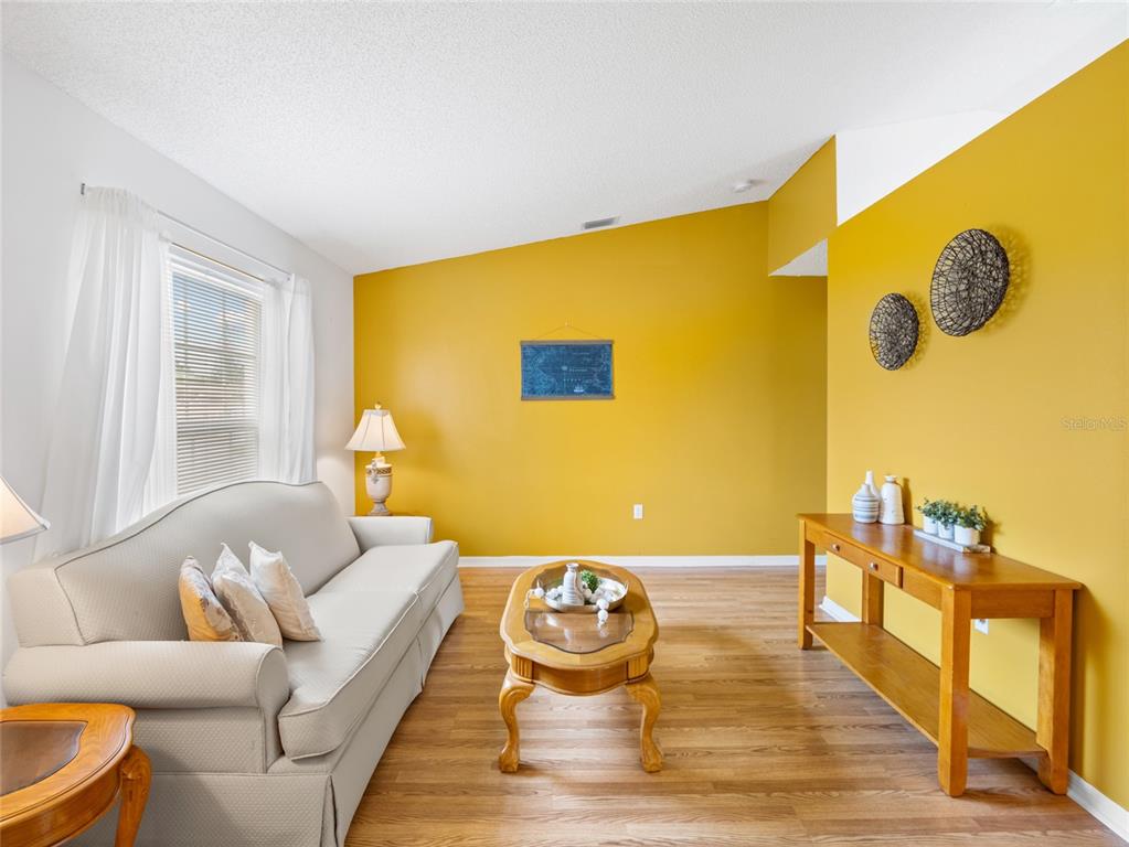 A living room features a light-colored sofa, wood coffee table, console table, and yellow walls — 867 NE FAIRHAVEN, PALM BAY, FL