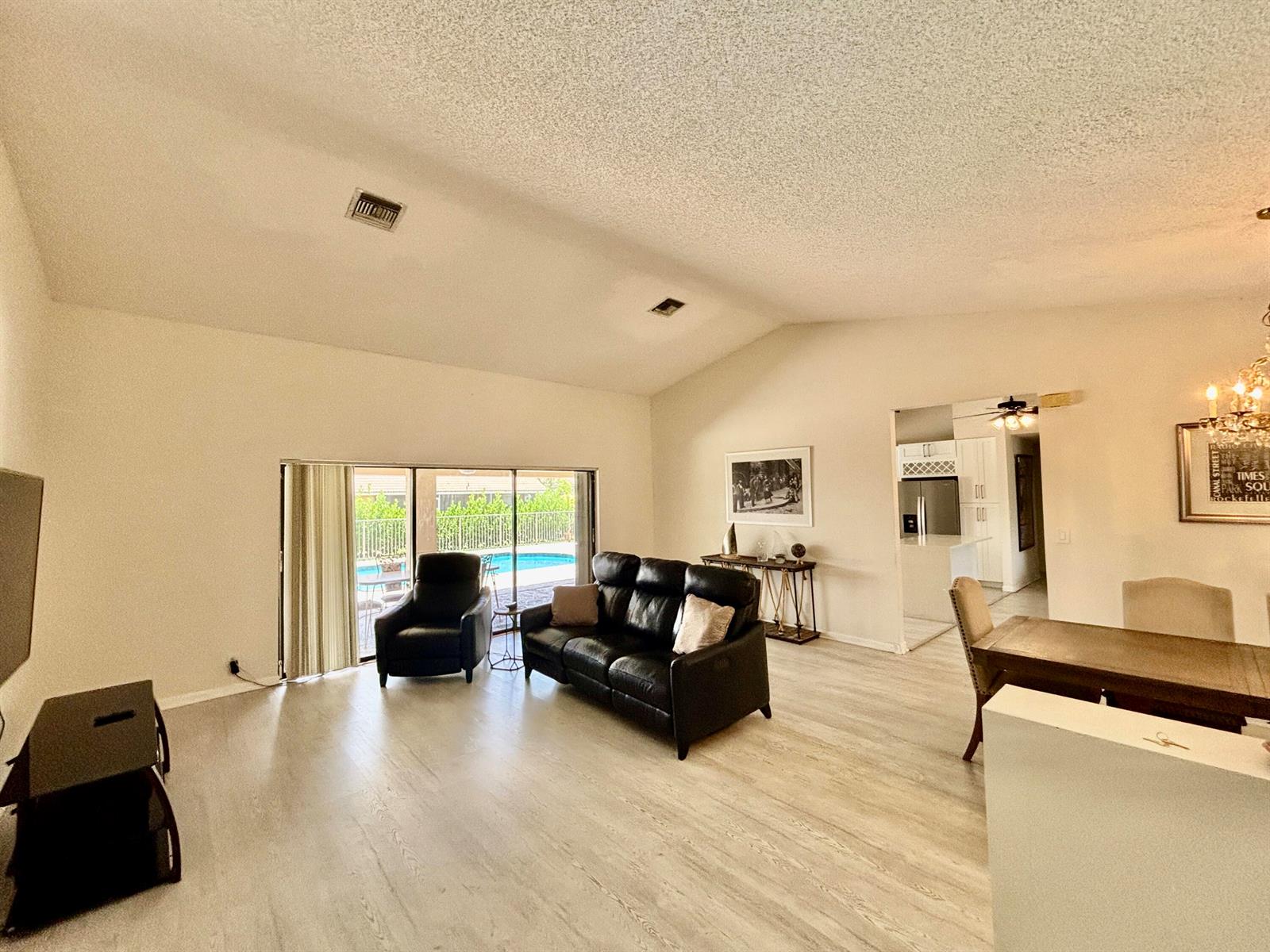A living room with vaulted ceilings, light wood flooring, and a view of a pool — 2153 Amesbury Circle, Wellington FL 33414, WELLINGTON, FL