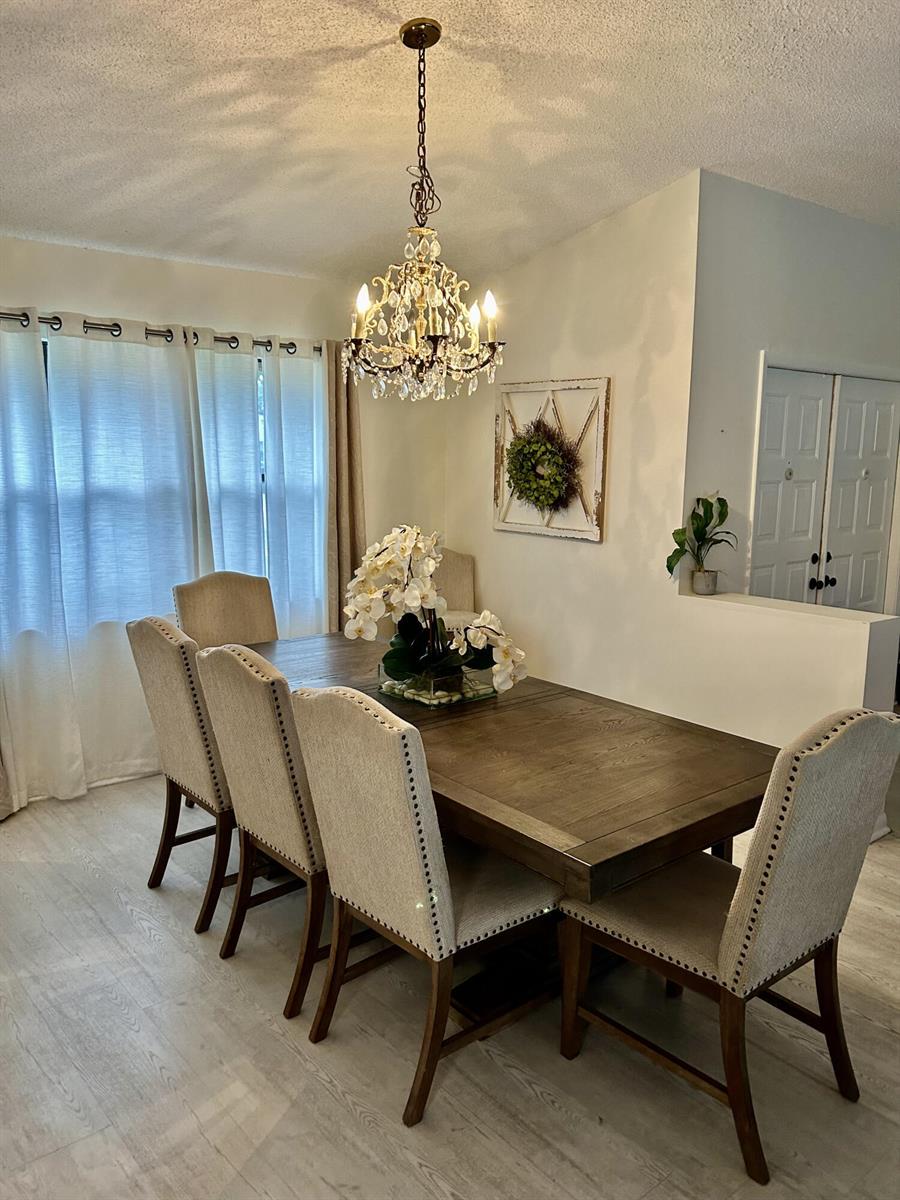 A dining room features a wooden table, upholstered chairs, a crystal chandelier, and sheer curtains — 2153 Amesbury Circle, Wellington FL 33414, WELLINGTON, FL