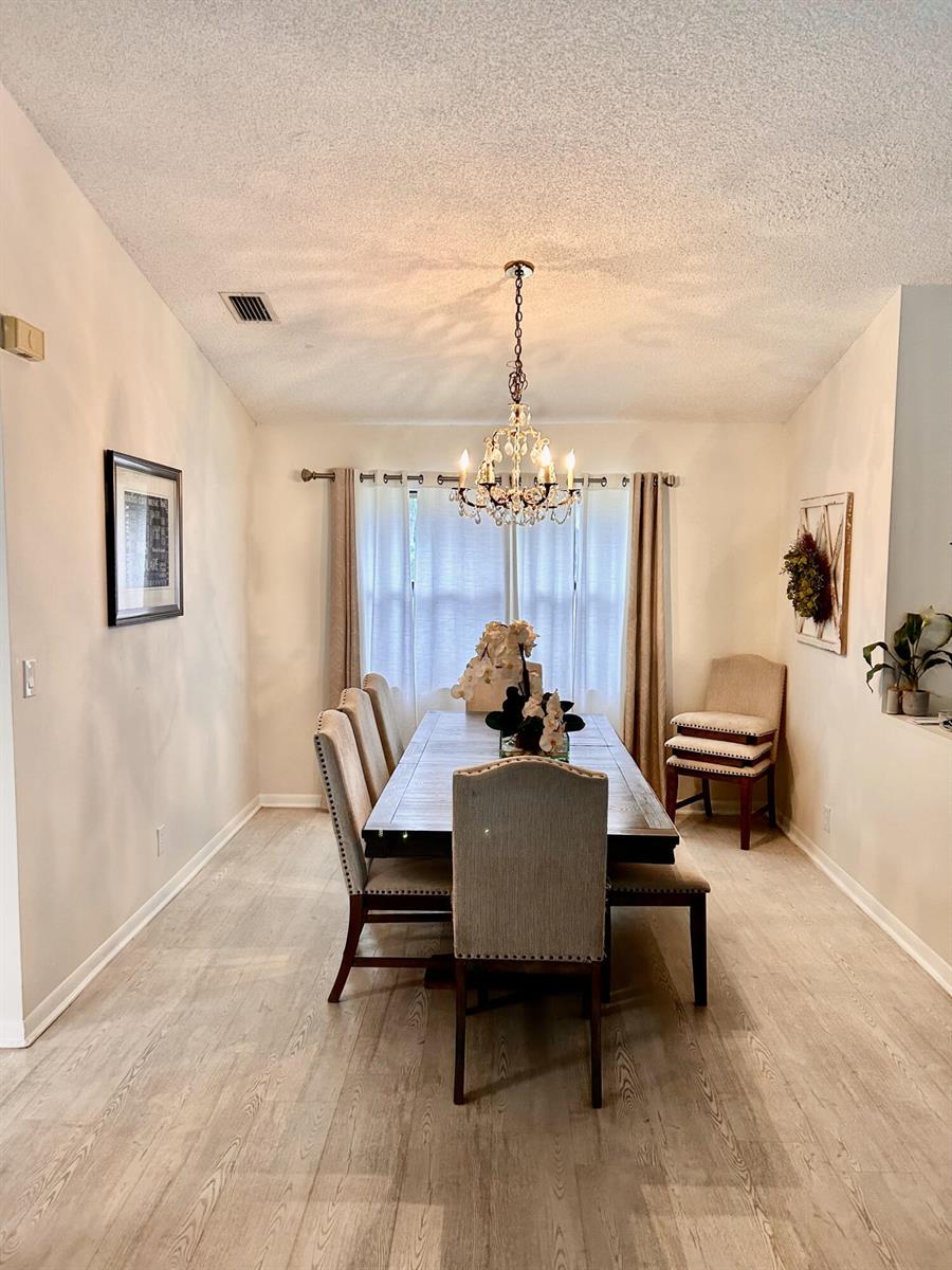 A dining room features a wooden table, upholstered chairs, a crystal chandelier, and light flooring — 2153 Amesbury Circle, Wellington FL 33414, WELLINGTON, FL