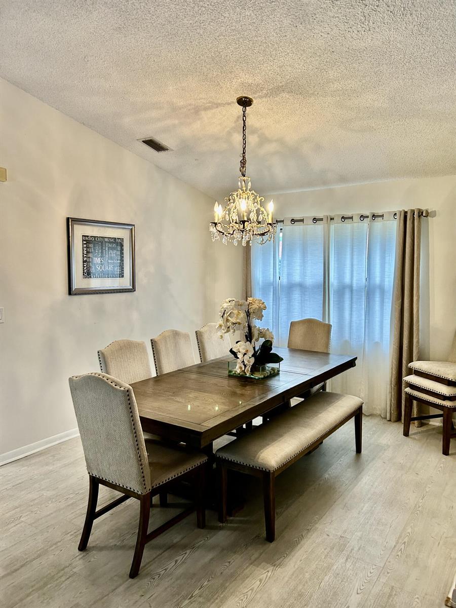 A dining room features a wooden table with chairs and a bench under a chandelier — 2153 Amesbury Circle, Wellington FL 33414, WELLINGTON, FL