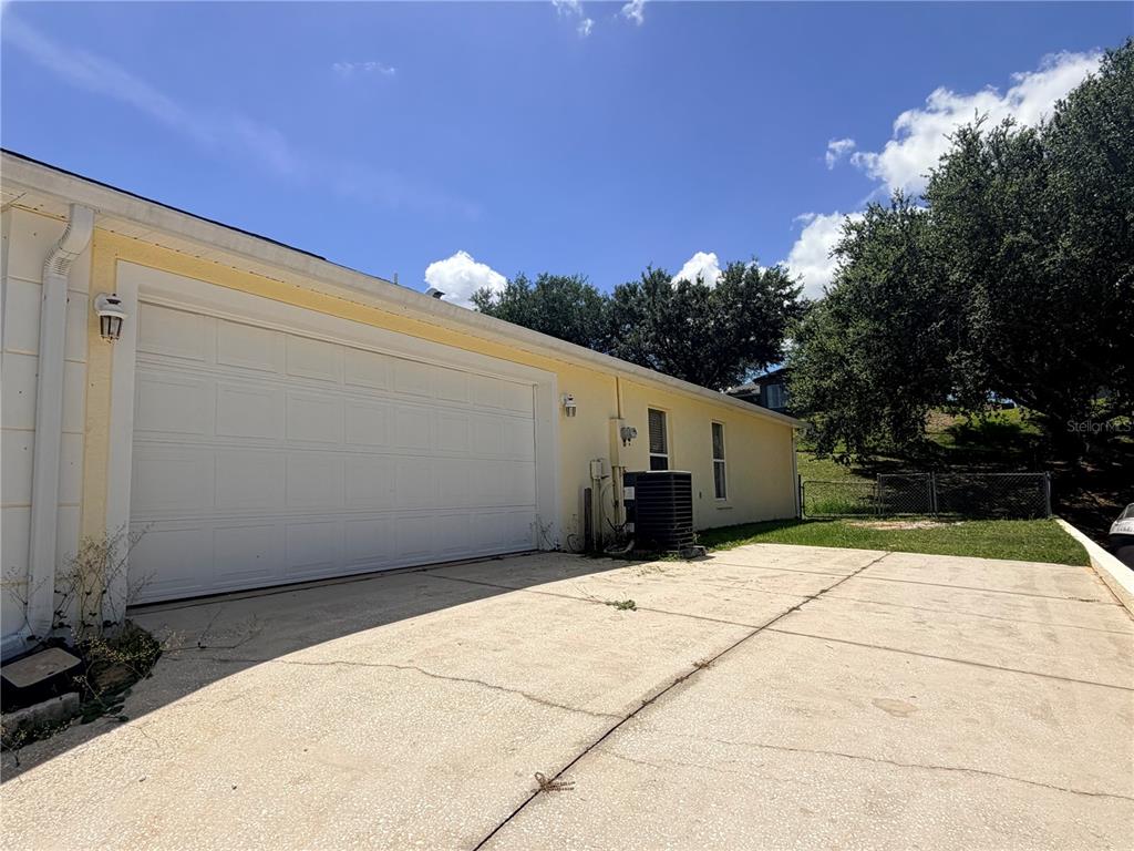 A yellow house exterior features a white garage door and a concrete driveway — 1011 SCENIC VIEW CIRCLE, MINNEOLA, FL