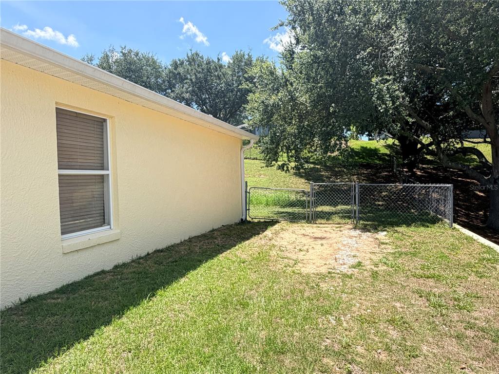 The exterior side of a yellow house features a window and a chain-link fence — 1011 SCENIC VIEW CIRCLE, MINNEOLA, FL
