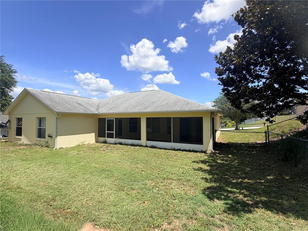 The exterior of a yellow house features a screened-in porch and a grassy backyard — 1011 SCENIC VIEW CIRCLE, MINNEOLA, FL