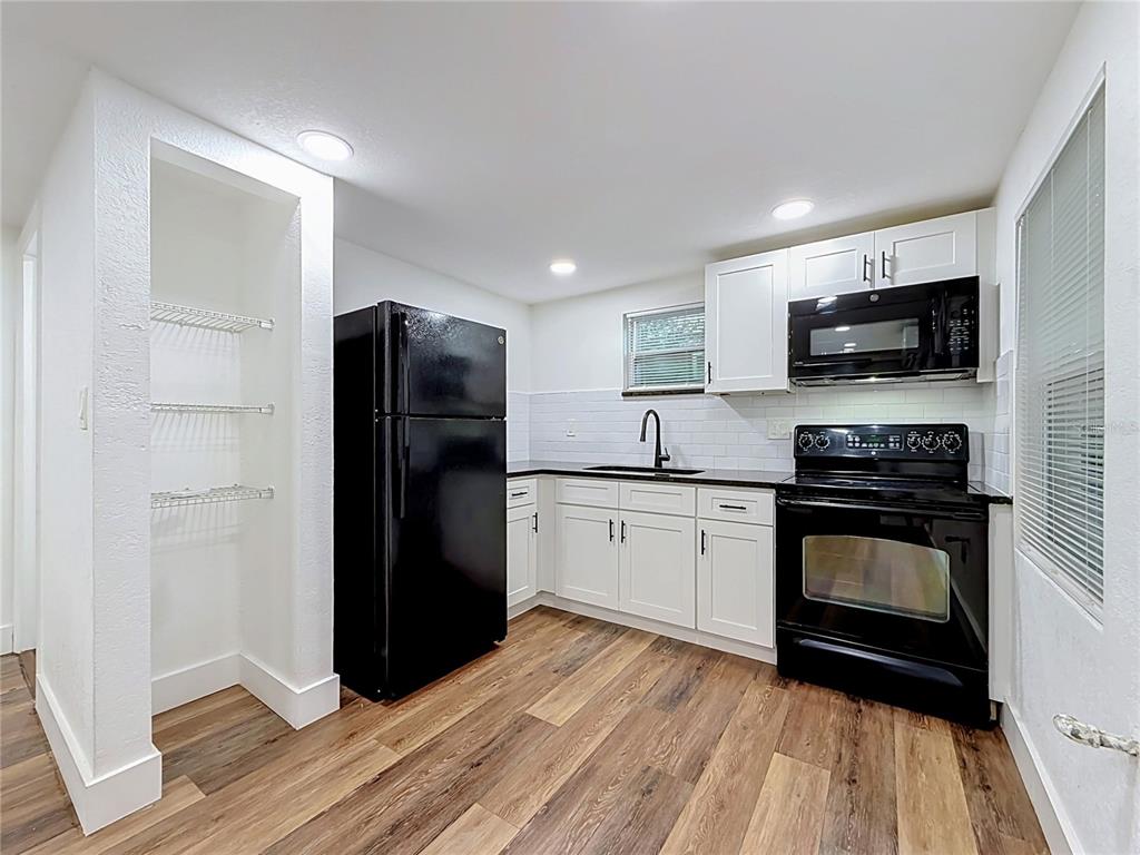 A kitchen features white cabinets, black appliances, a subway tile backsplash, and wood-look flooring — 800 15TH AVENUE S, ST PETERSBURG, FL