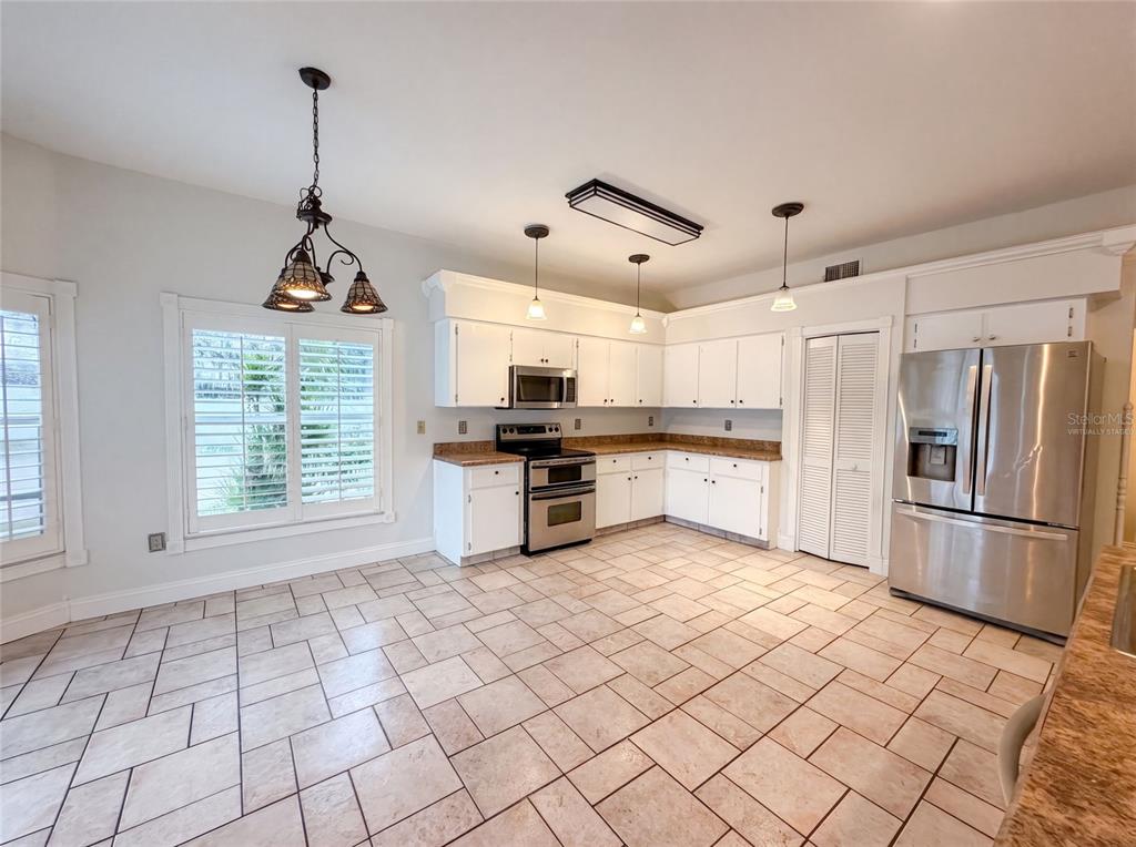 A kitchen features white cabinetry, stainless steel appliances, and light-colored tile flooring — 1701 LARABIE COURT, BRANDON, FL