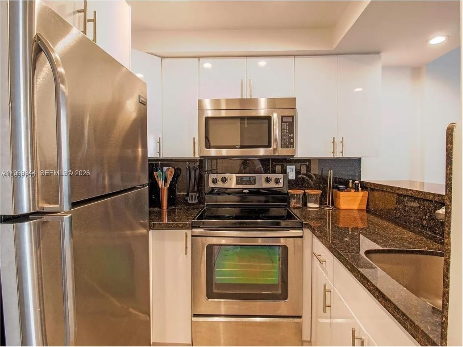 A kitchen features stainless steel appliances, white cabinetry, and dark granite countertops — 1035 West Ave # 802, Miami Beach FL 33139, MIAMI BEACH, FL