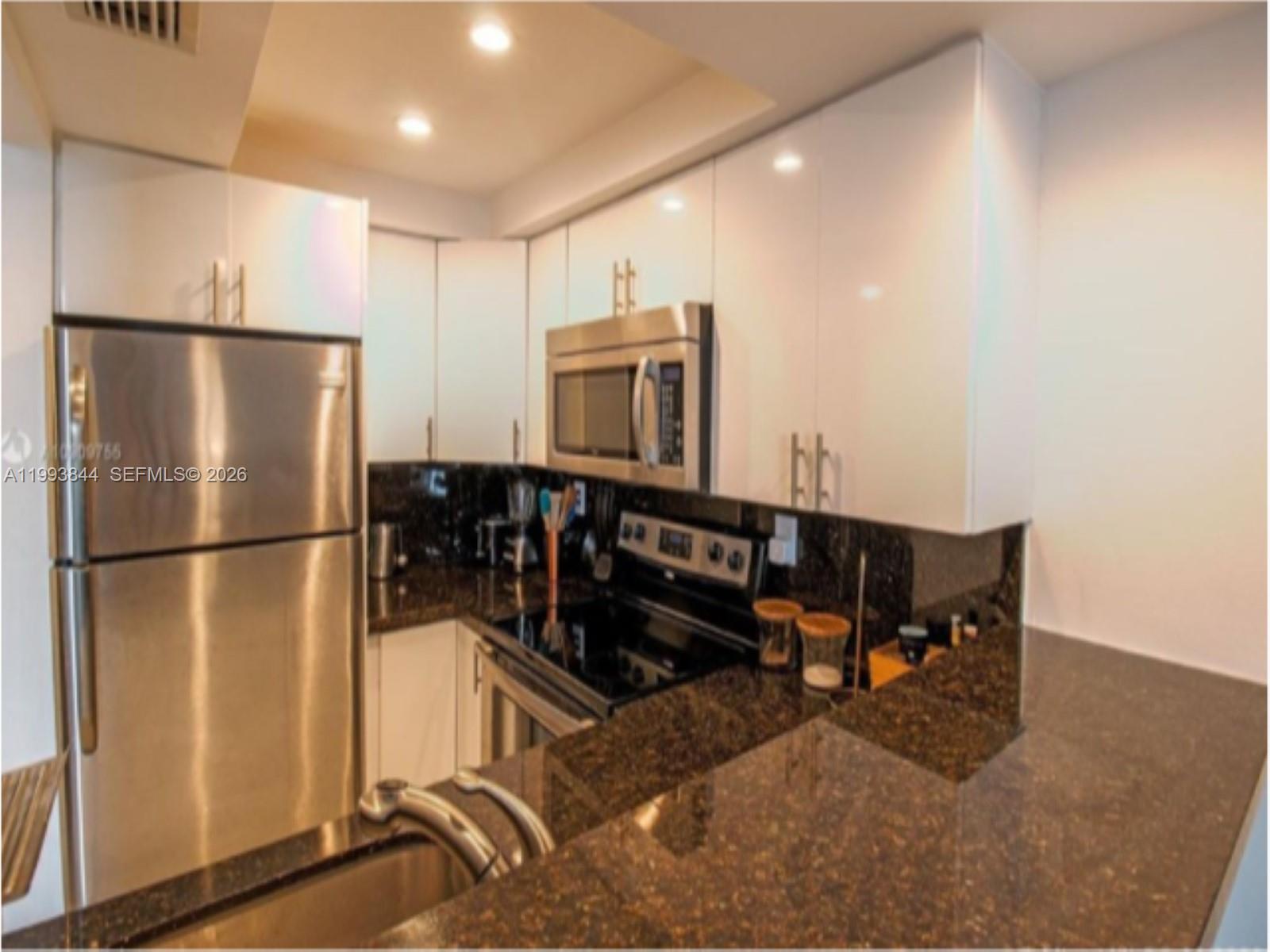 A kitchen features white cabinets, stainless steel appliances, and dark granite countertops — 1035 West Ave # 802, Miami Beach FL 33139, MIAMI BEACH, FL
