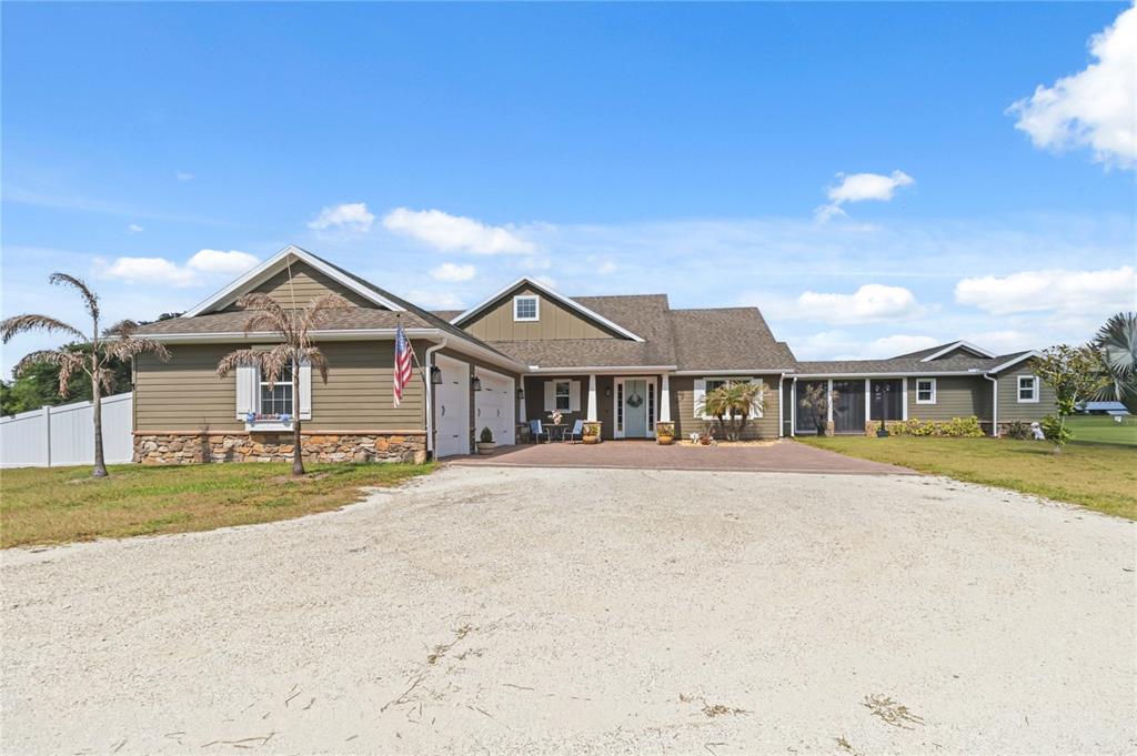 A single-story house with olive-green siding, a stone base, and a large gravel driveway — 4901 MANOR HOUSE LANE, ST CLOUD, FL