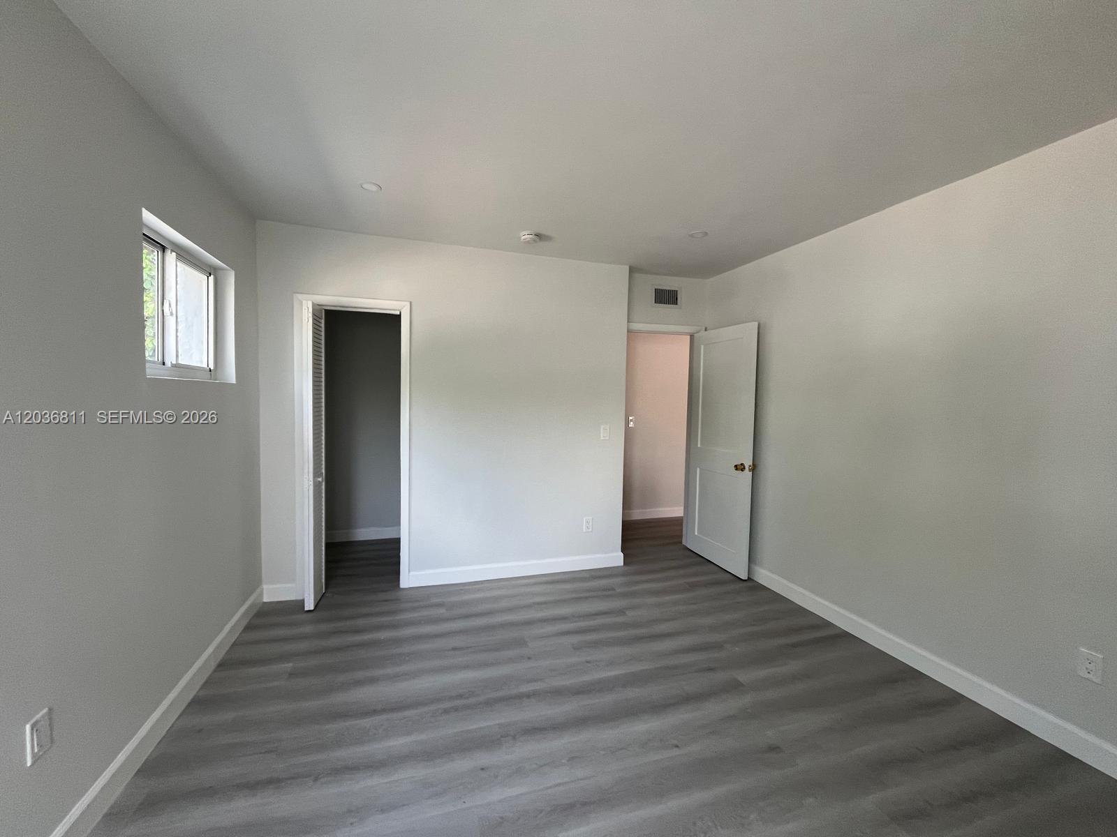 An empty room features light gray walls, wood-look flooring, two doorways, and a small window — 602 SW 13th Ave # 4, Miami FL 33135, MIAMI, FL
