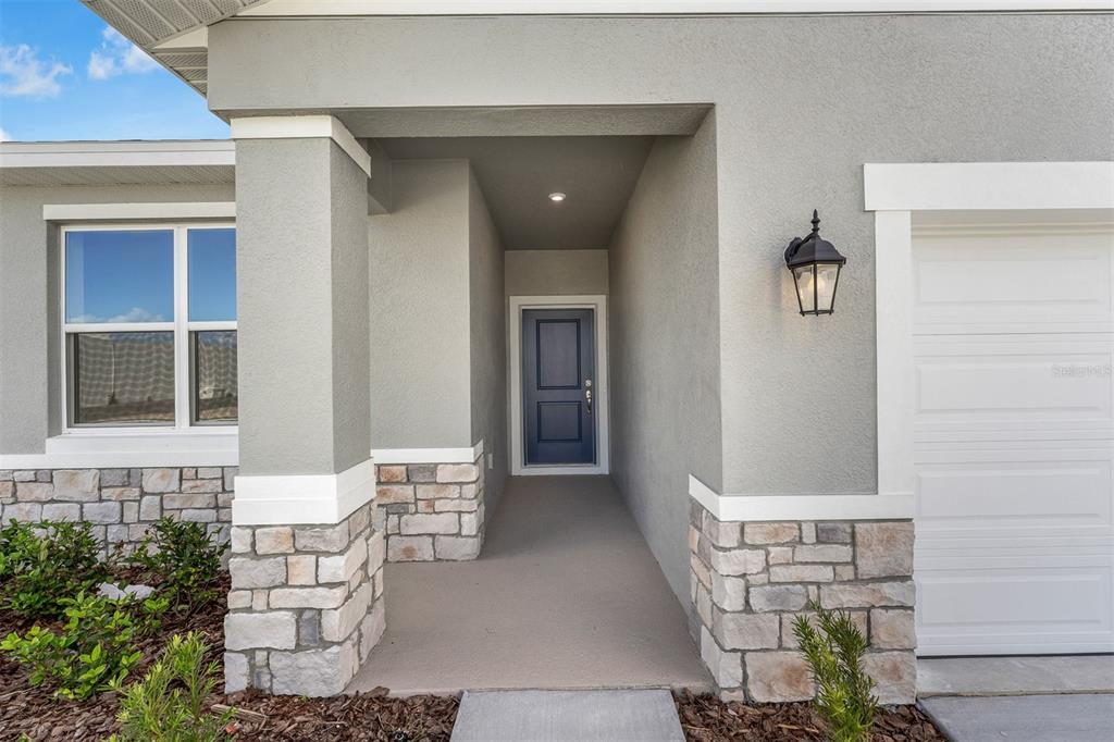 A gray house exterior features a stone-accented porch, a blue front door, and a garage — 6747 WINTERBERRY DRIVE, LAKE HAMILTON, FL