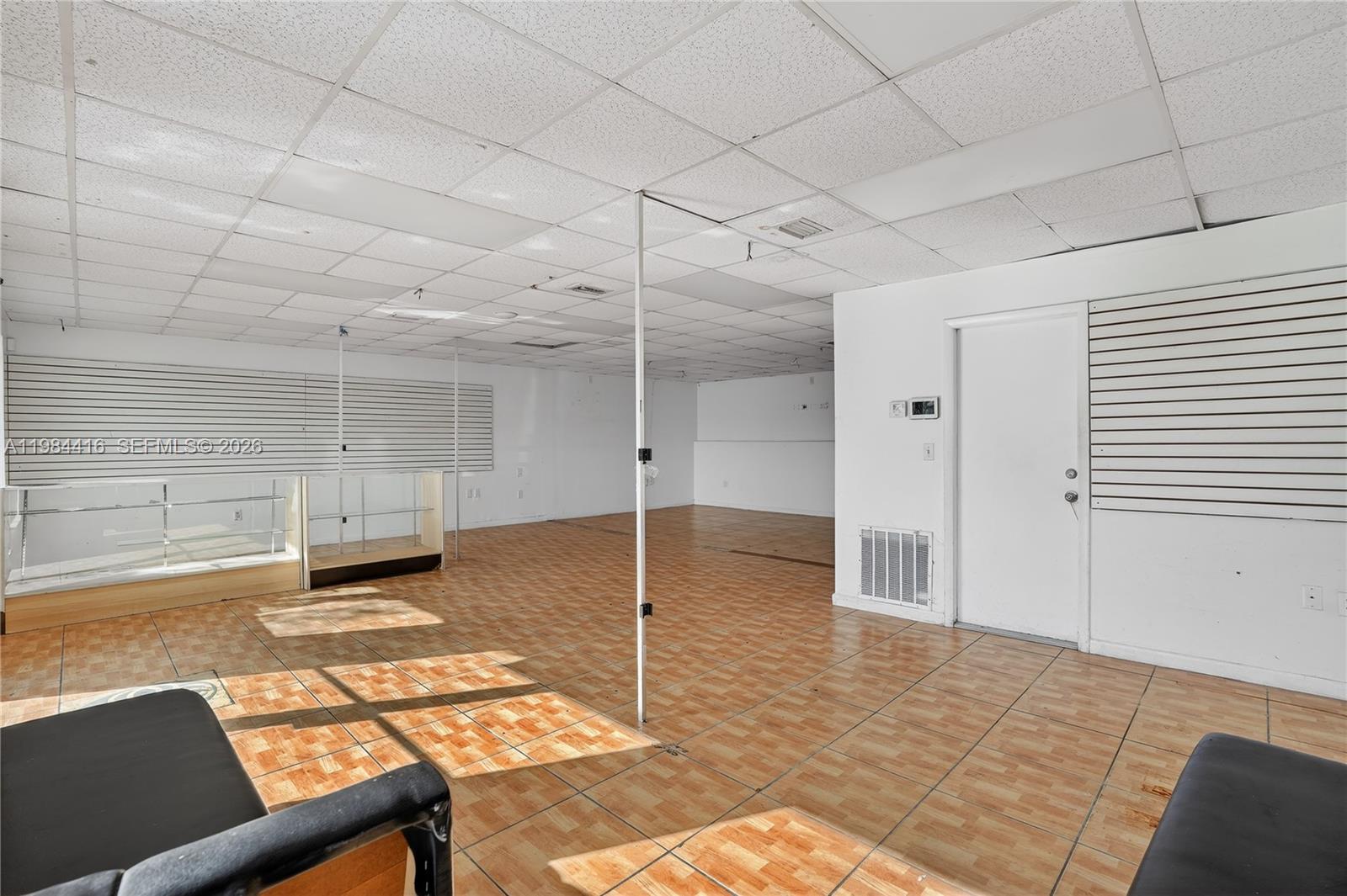 An empty commercial space features a drop ceiling, tiled flooring, and wall-mounted slat panels — 200 SW 57th AVE, FL 33144, FL