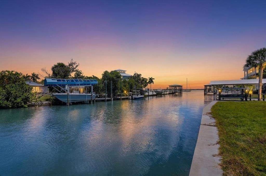 A canal view at sunset featuring boat lifts, docks, and lush tropical landscaping — 180 MOCKINGBIRD LANE, ENGLEWOOD, FL