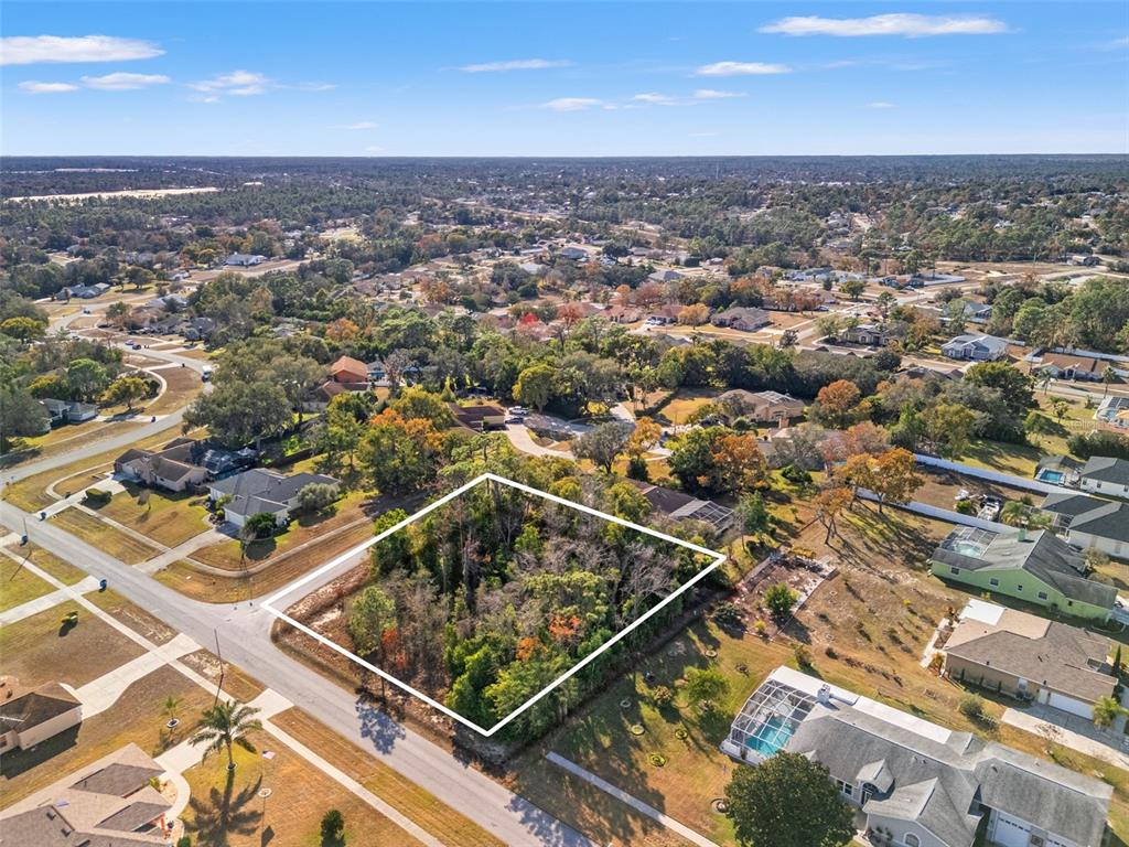 An aerial view shows a vacant, wooded residential lot outlined in white within a suburban neighborhood — SEBASTIAN DRIVE, SPRING HILL, FL