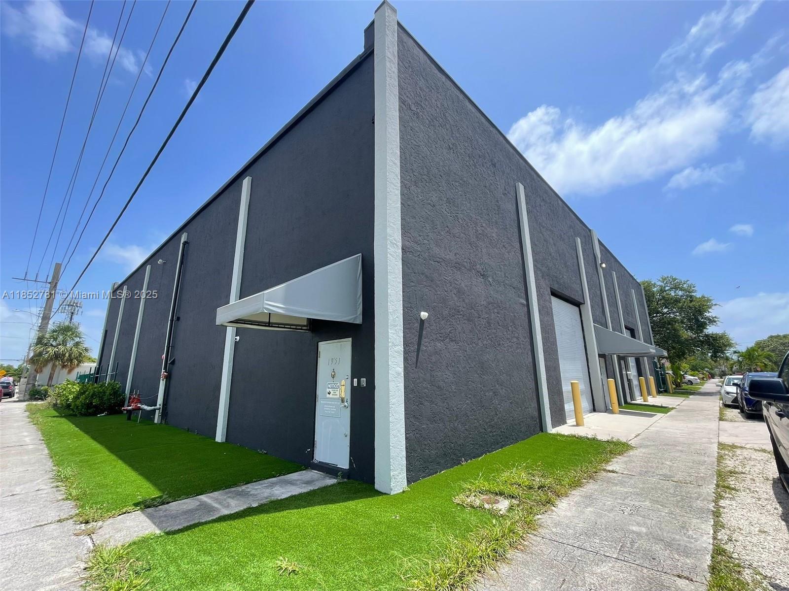 A dark gray industrial building features a white entrance door and a roll-up garage door — 1951 Grant St, Hollywood FL 33020, HOLLYWOOD, FL