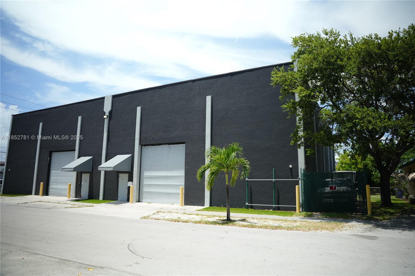 A black industrial warehouse building features two roll-up doors, metal awnings, and a fenced area — 1951 Grant St, Hollywood FL 33020, HOLLYWOOD, FL