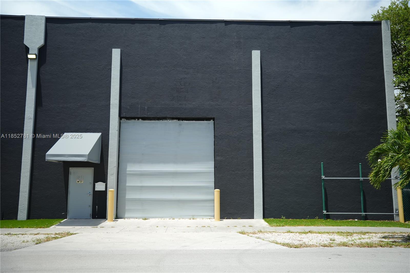 The exterior of a commercial building features a black wall, a gray roll-up door, and a door — 1951 Grant St, Hollywood FL 33020, HOLLYWOOD, FL