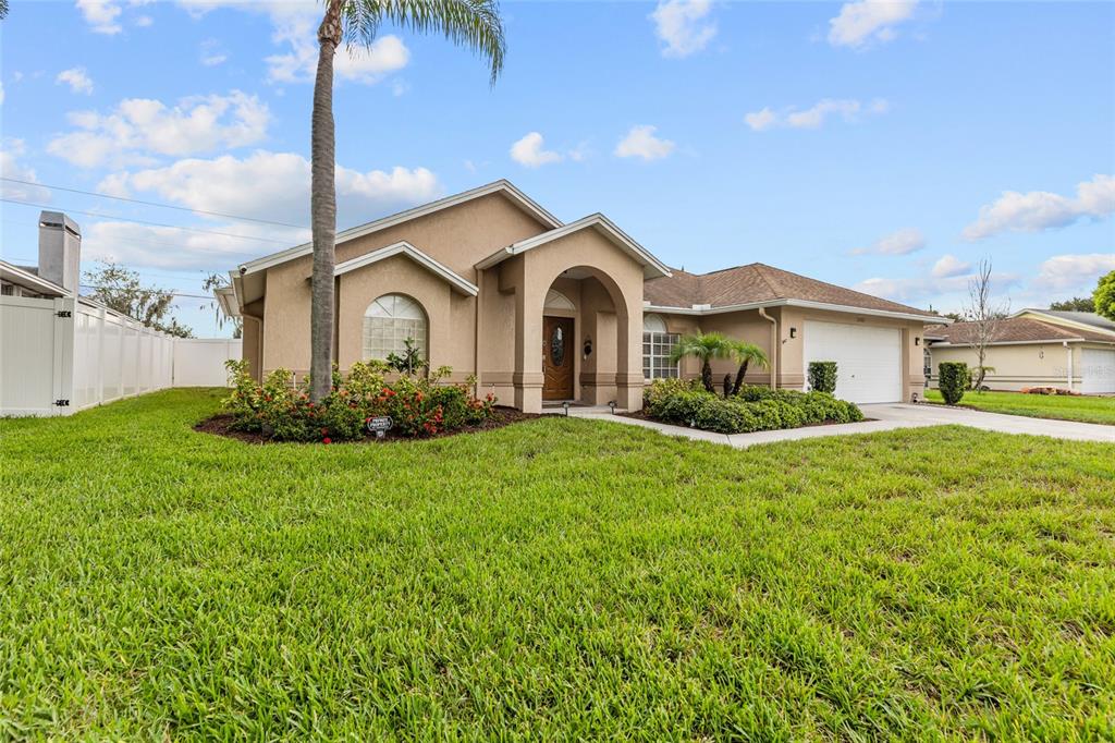 A single-story tan stucco house with a palm tree, arched entryway, and two-car garage — 22861 STERLING MANOR LOOP, LUTZ, FL