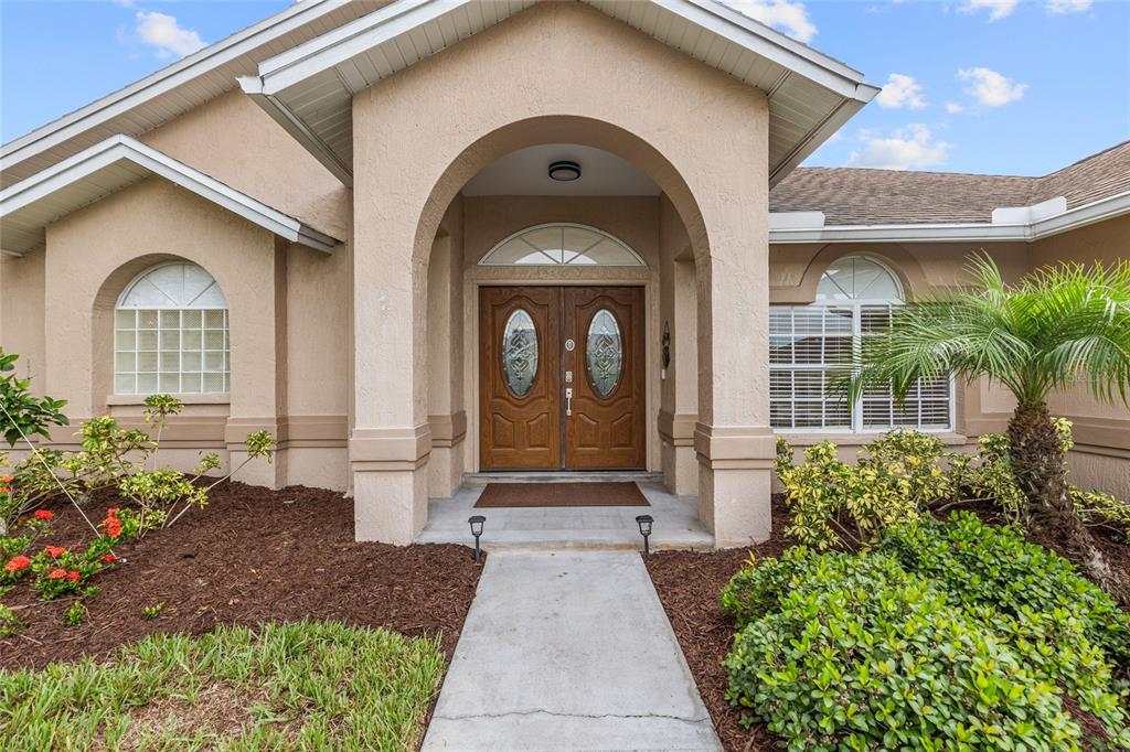 The exterior of a house features a concrete walkway leading to a double-door arched entryway — 22861 STERLING MANOR LOOP, LUTZ, FL