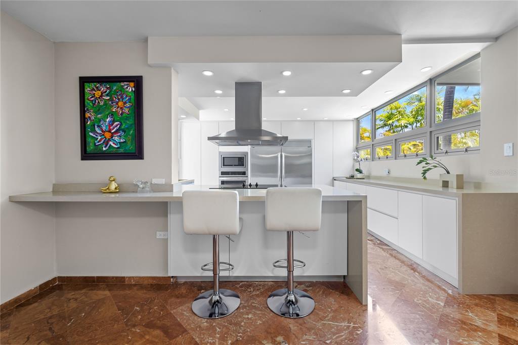 A modern kitchen features white cabinetry, a central island with bar stools, and marble flooring — 69 ROBLE, GUAYNABO, PR