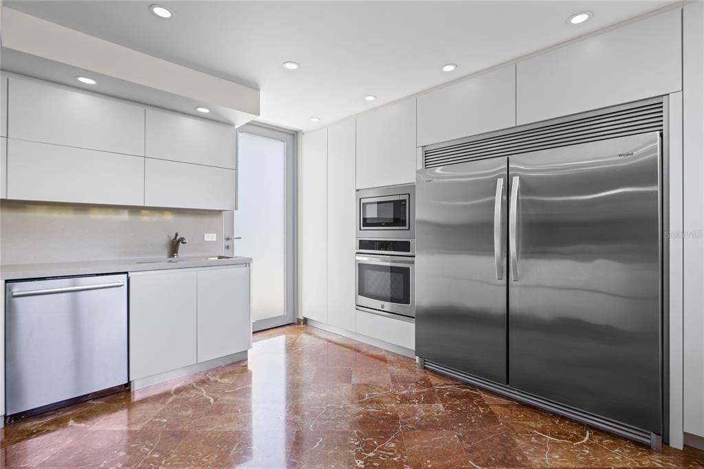 A modern kitchen features white cabinetry, stainless steel appliances, and polished reddish-brown marble flooring — 69 ROBLE, GUAYNABO, PR