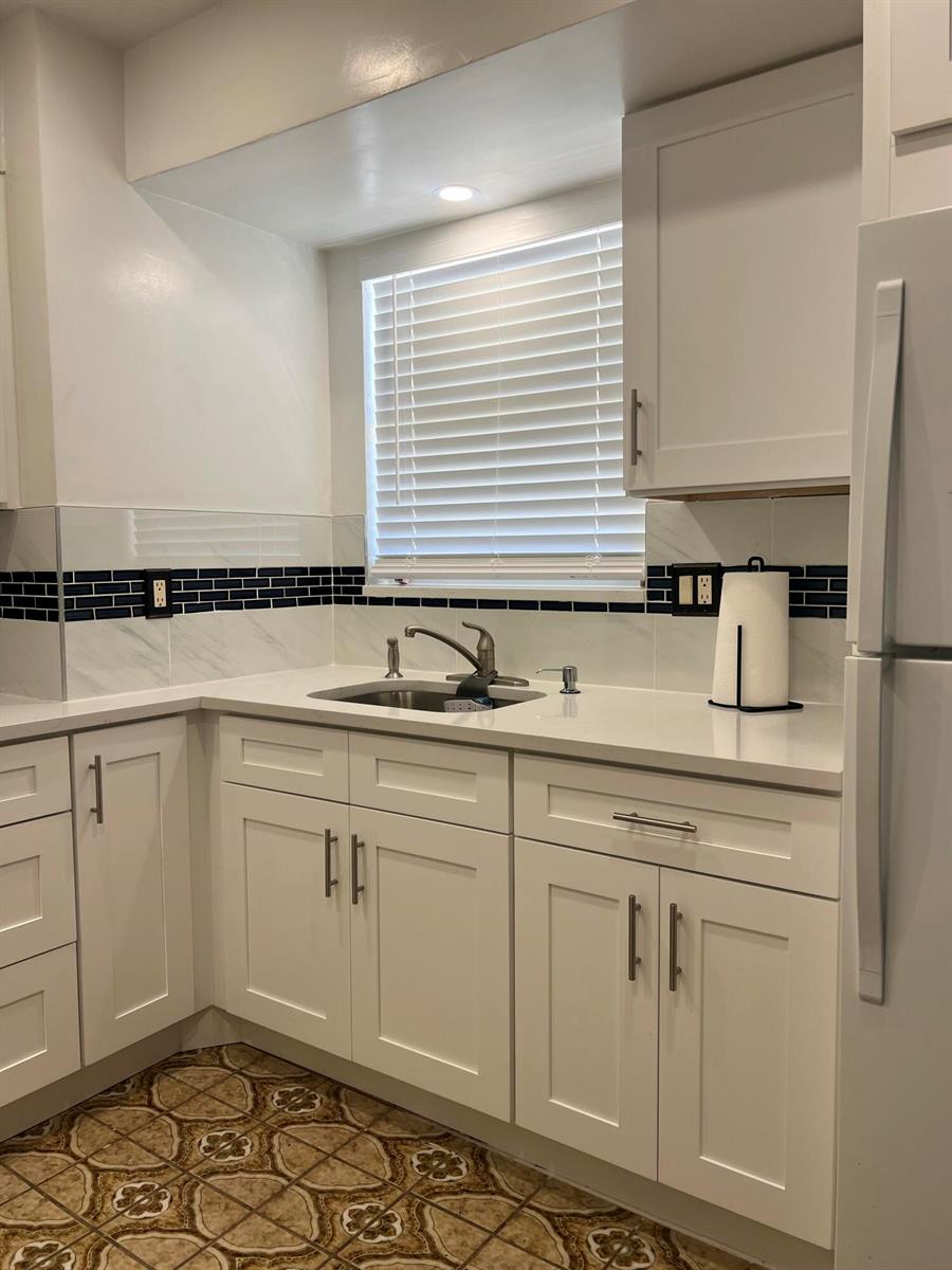 A kitchen features white cabinets, quartz countertops, a dark tile backsplash, and patterned floor tiles — 719 Lori Drive # 203, Palm Springs FL 33461, PALM SPRINGS, FL