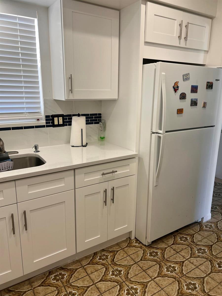A kitchen features white cabinets, a white refrigerator, a stainless steel sink, and patterned flooring — 719 Lori Drive # 203, Palm Springs FL 33461, PALM SPRINGS, FL