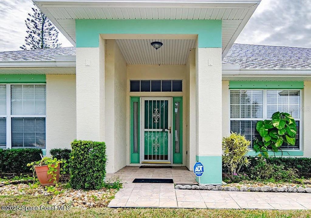 The exterior of a house features a covered entryway with a teal-trimmed door and windows — 778 NW HAMM STREET, PALM BAY, FL