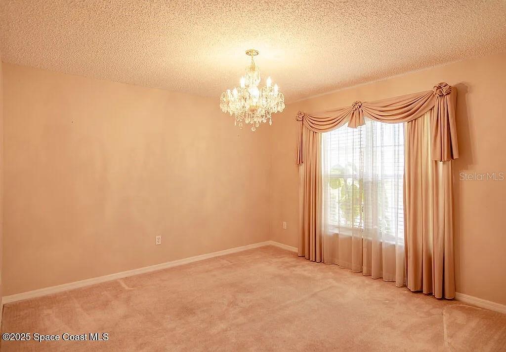 An empty room features beige walls, carpeted flooring, a crystal chandelier, and draped window curtains — 778 NW HAMM STREET, PALM BAY, FL