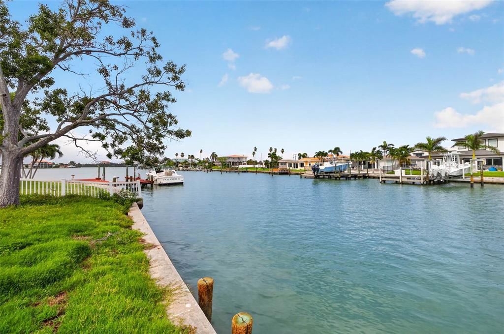 A grassy waterfront yard overlooks a canal with several docked boats and residential homes — 643 NORMANDY ROAD, MADEIRA BEACH, FL
