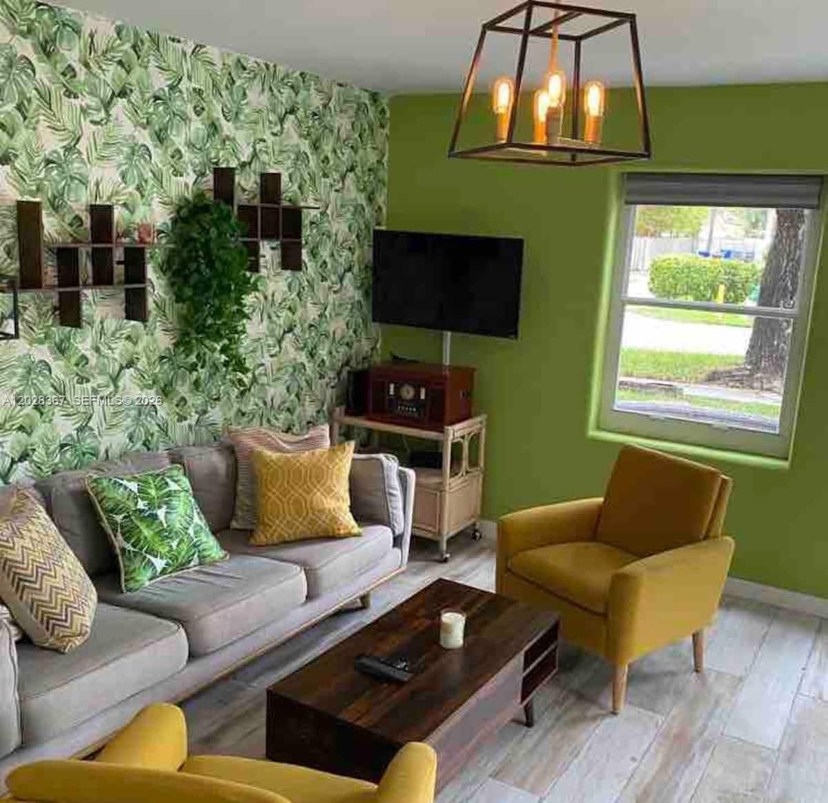 A living room features a palm-leaf wallpaper accent wall, green paint, and yellow armchairs — 1516 S 17th Ave # 1516, Hollywood FL 33020, HOLLYWOOD, FL