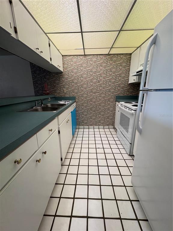 A galley kitchen features white cabinets, green countertops, floral wallpaper, and a tiled floor — 167 PALM VIEW COURT UNIT 3487, HAINES CITY, FL