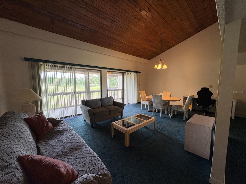 A living and dining room with a vaulted wood ceiling, blue carpet, and sliding glass doors — 167 PALM VIEW COURT UNIT 3487, HAINES CITY, FL