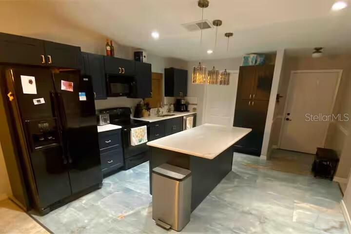 A kitchen features dark cabinetry, a white-topped island, stainless steel appliances, and light-colored flooring — 6338 51ST AVENUE N UNIT 0, ST PETERSBURG, FL