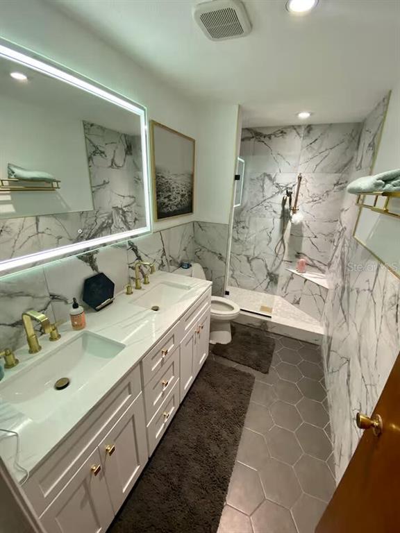 A bathroom features a white vanity, marble-style tile walls, a walk-in shower, and gray flooring — 6338 51ST AVENUE N UNIT 0, ST PETERSBURG, FL