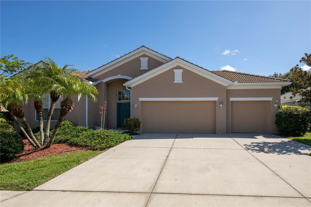 A single-story house with a tan stucco exterior, a three-car garage, and a palm tree — 1679 PINYON PINE DRIVE, SARASOTA, FL