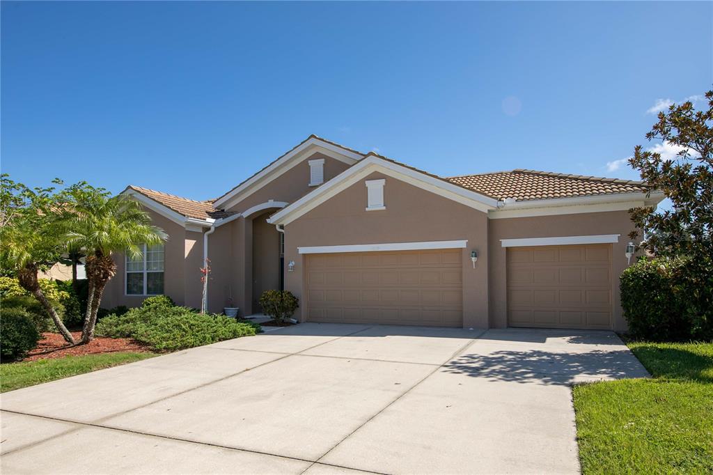 A single-story house with a tan stucco exterior, a tile roof, and a three-car garage — 1679 PINYON PINE DRIVE, SARASOTA, FL