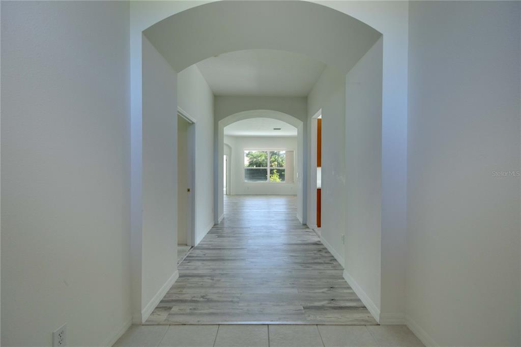 A hallway with arched entryways leads to a room with light wood-look flooring — 1679 PINYON PINE DRIVE, SARASOTA, FL