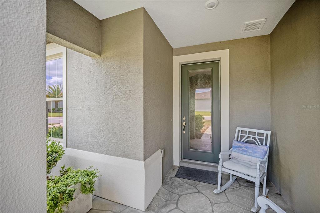 A covered front porch features a gray door, stone flooring, and a white rocking chair — 6276 SW 93RD TERRACE, OCALA, FL