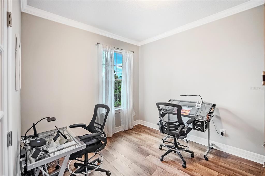 A home office with wood-look flooring, two glass-top drafting desks, and a window with curtains — 6276 SW 93RD TERRACE, OCALA, FL