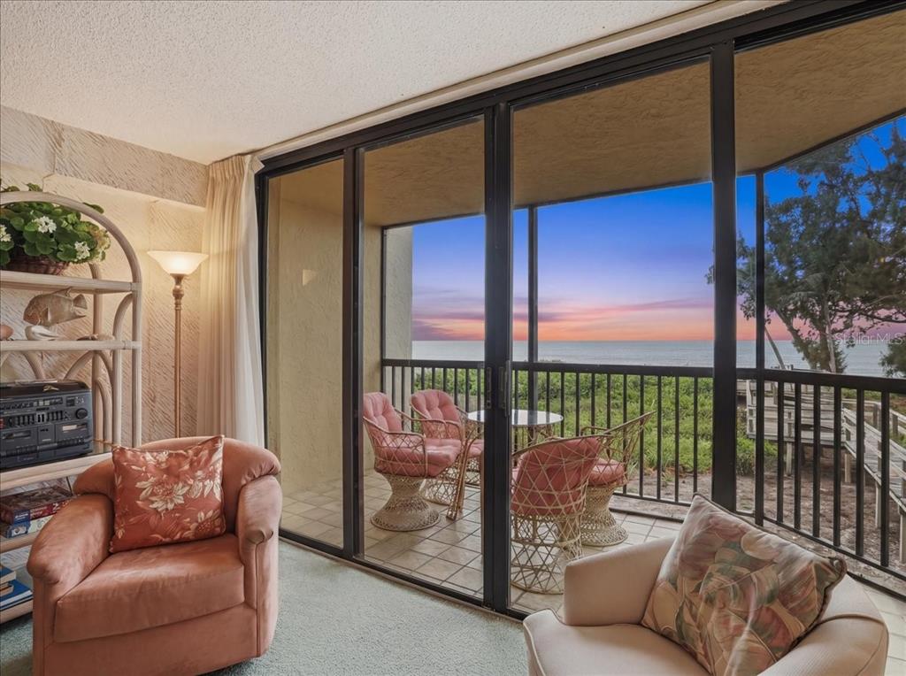 A living room with two armchairs overlooks a balcony with ocean views at sunset — 5611 GULF OF MEXICO DRIVE UNIT 3, LONGBOAT KEY, FL