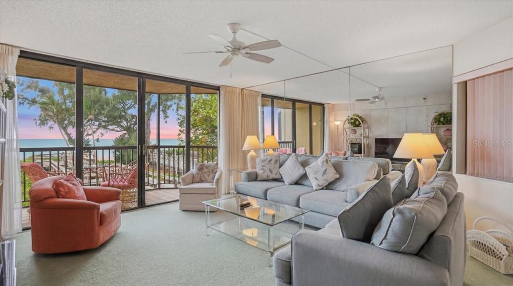 A living room with a gray sectional, an orange chair, and a mirrored wall overlooking water — 5611 GULF OF MEXICO DRIVE UNIT 3, LONGBOAT KEY, FL