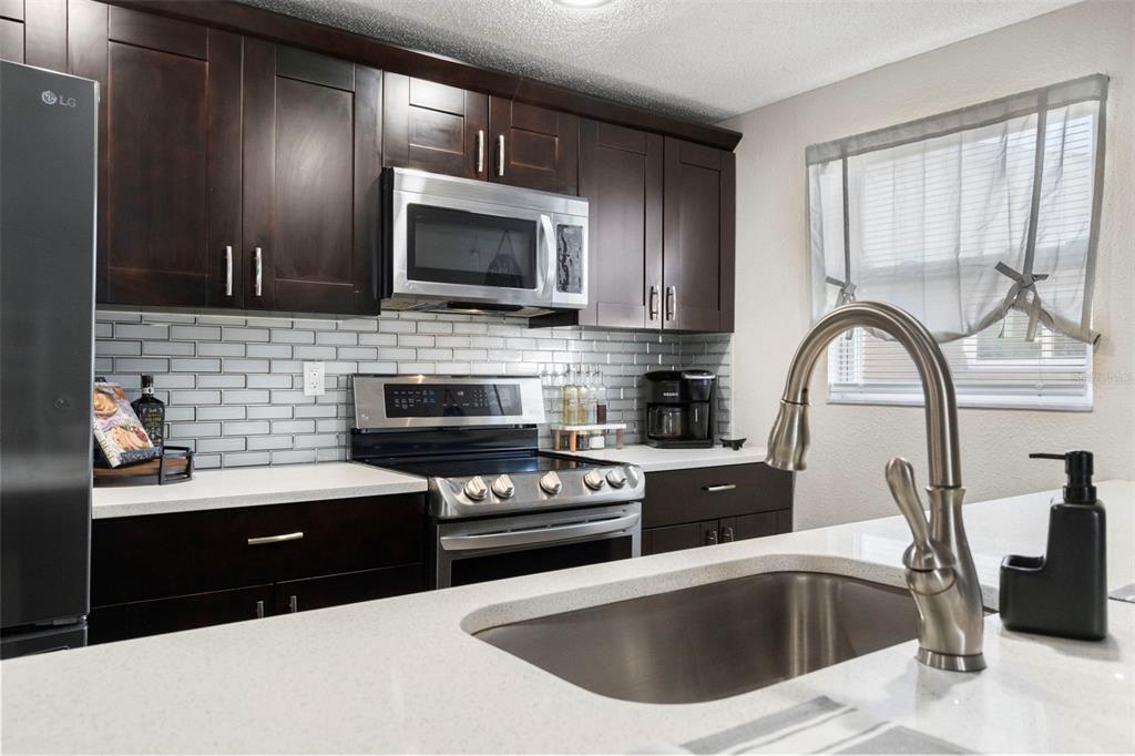 A kitchen features dark wood cabinets, stainless steel appliances, white countertops, and a subway tile backsplash — 6333 ABERDEEN AVENUE, NEW PORT RICHEY, FL