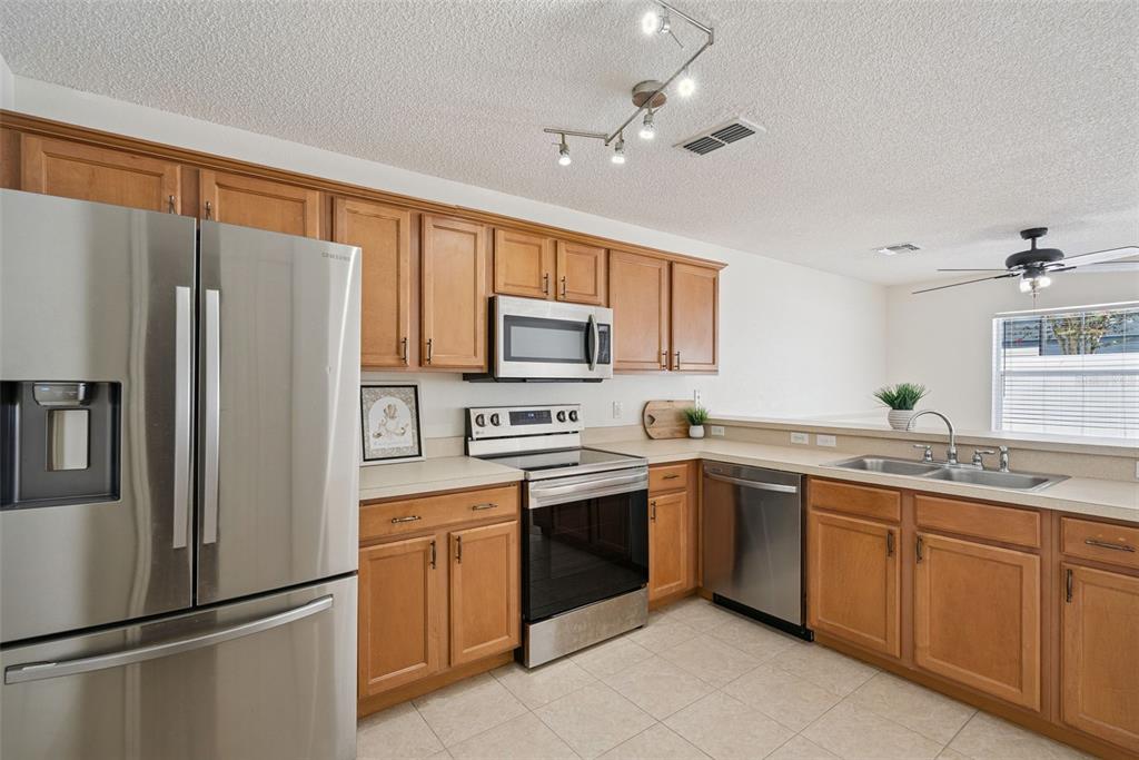 A kitchen with wood cabinets, stainless steel appliances, and tile flooring opens to a living area — 12621 SOMERSET OAKS STREET, ORLANDO, FL