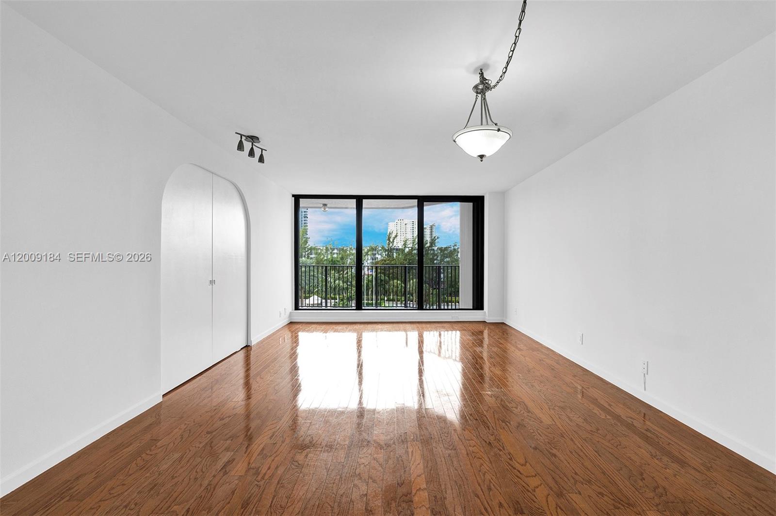 An empty room features hardwood floors, white walls, a hanging light fixture, and large windows — 300 Three Islands Blvd # 305, Hallandale Beach FL 33009, HALLANDALE BEACH, FL