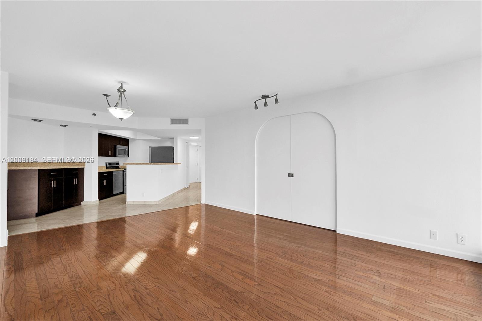 A living room with hardwood floors features an arched double-door closet and an adjacent kitchen — 300 Three Islands Blvd # 305, Hallandale Beach FL 33009, HALLANDALE BEACH, FL