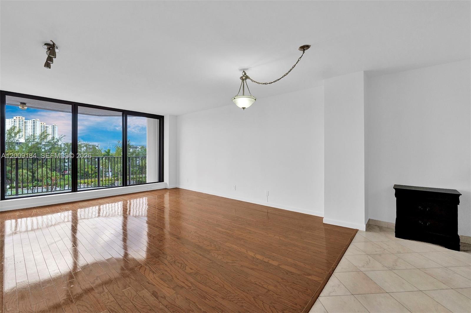 A living room features hardwood flooring, a hanging light fixture, and a balcony with views — 300 Three Islands Blvd # 305, Hallandale Beach FL 33009, HALLANDALE BEACH, FL