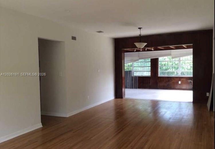 An interior view shows a living room with hardwood floors and a wood-paneled sunroom beyond — 730 NE 139 ST, North Miami FL 33161, NORTH MIAMI, FL