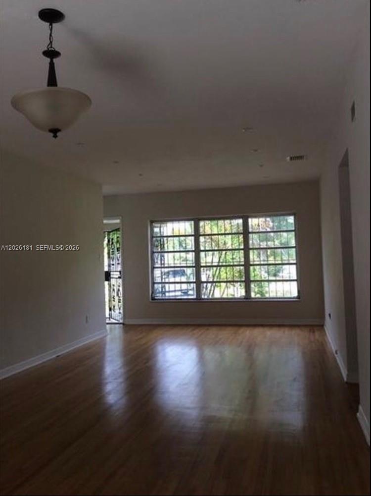 An empty living room features hardwood floors, a hanging light fixture, and a large window — 730 NE 139 ST, North Miami FL 33161, NORTH MIAMI, FL